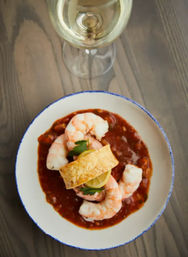 Plump shrimp cocktail seafood appetizer in zesty tomato-based sauce, lemon slice and parsley garnish with a crusty crostini and a glass of white wine on a rustic wooden table