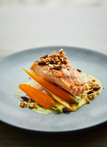Grilled salmon fillet on a creamy herb sauce with glazed carrots and crunchy walnut crumble, plated fine-dining style