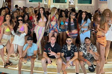 Large group of young adults in swimsuits and colorful summer outfits posing on illuminated steps inside a lively hotel or nightclub, upbeat summer party vibe.
