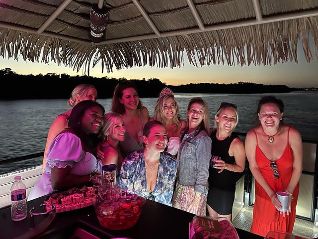 Smiling group of friends enjoying a sunset boat party under a tiki thatched canopy on a calm river, drinks and a punch bowl on the table