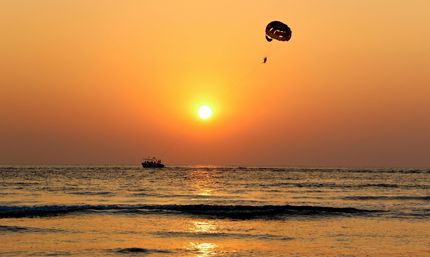 Golden coastal sunset with a silhouetted boat towing a parasailor over calm ocean waves and the sun reflecting on the water