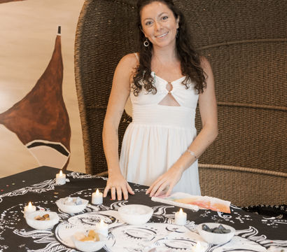 Smiling woman in a white dress at a boho wellness table with crystals, lit candles, and sun-and-moon tapestry in a cozy indoor studio