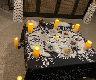 Indoor bohemian crystal altar on a sun-and-moon tapestry with LED candles, bowls of polished healing stones and selenite wands.