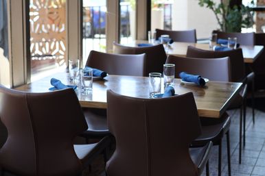 Sunlit restaurant interior with wooden dining tables, brown leather chairs, blue rolled napkins and glassware set for casual dining.