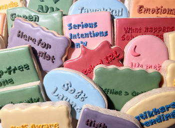 Close-up of pastel iced sugar cookies in assorted shapes, decorated with colorful lettered icing messages and playful designs — a bright, bakery-style cookie assortment.