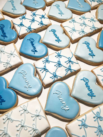 Assorted pastel blue heart-shaped and white rectangular iced sugar cookies with blue piped bows and personalized cursive script on a white background