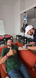Man on orange couch gives thumbs up while a gloved technician prepares an IV drip for home IV therapy in a modern apartment living room.
