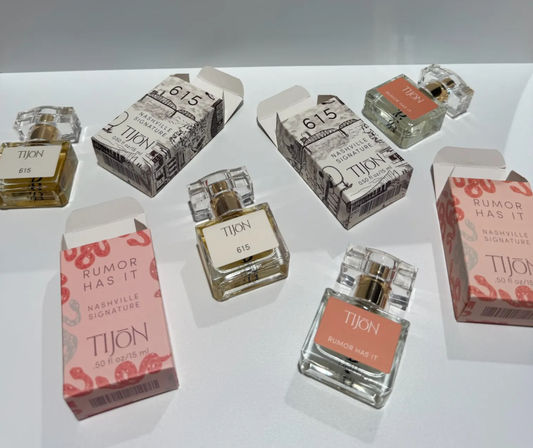 Flat-lay retail display of small clear perfume sample bottles with gold pumps and coordinating pink and illustrated boxes on a white surface