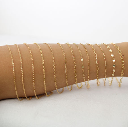 Dainty gold chain bracelets stacked along a forearm on a clean white background — minimalist jewelry display, close-up