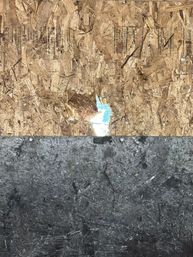 Boarded construction surface: rough OSB plywood with a small tear revealing bright blue behind, above a dark weathered asphalt/tar panel with visible screws.