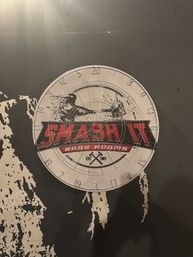 Round metal dartboard-style target sign with red banner and concentric rings mounted on a distressed black wall in an indoor entertainment space