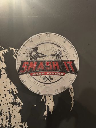 Round metal dartboard-style target sign with red banner and concentric rings mounted on a distressed black wall in an indoor entertainment space