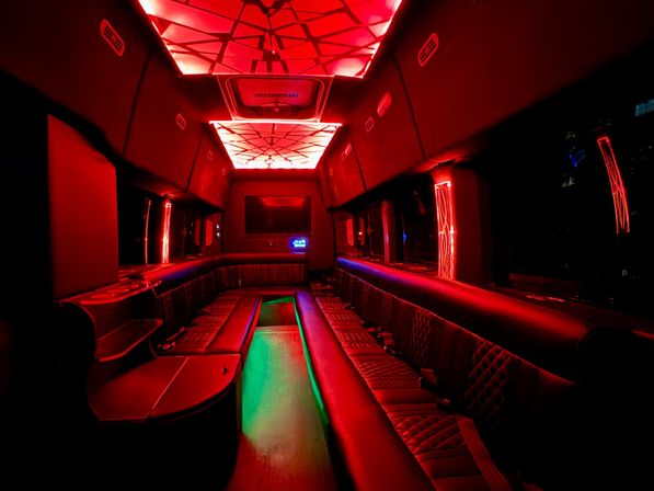 Neon-lit party bus interior with quilted leather bench seats, red geometric LED ceiling panels and a green-lit center aisle for nightlife rides