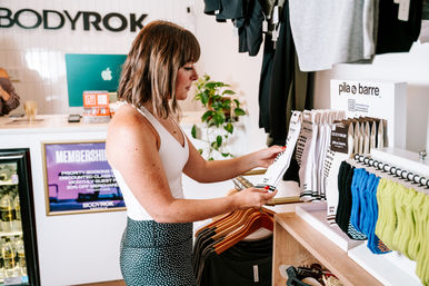 Shopper browsing anti-slip workout socks and activewear on display in a bright, modern boutique fitness studio retail area