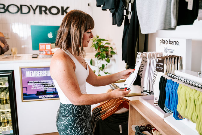 Shopper browsing anti-slip workout socks and activewear on display in a bright, modern boutique fitness studio retail area