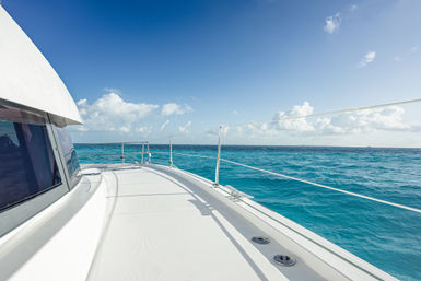 Sunlit yacht deck gliding across turquoise tropical sea under a bright blue sky with fluffy clouds on the horizon.