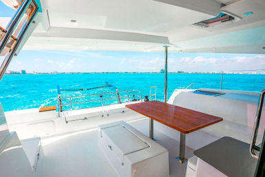 Luxurious yacht aft deck with wooden dining table and seating overlooking vibrant turquoise ocean and distant coastal skyline under a sunny blue sky