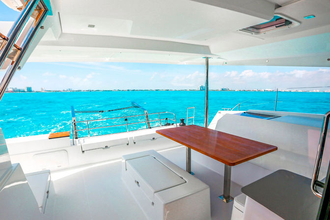 Luxurious yacht aft deck with wooden dining table and seating overlooking vibrant turquoise ocean and distant coastal skyline under a sunny blue sky