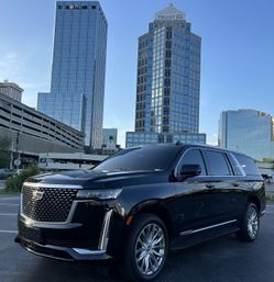 Sleek black luxury SUV with gleaming chrome accents parked in a downtown lot against a backdrop of reflective glass skyscrapers under a clear blue sky.