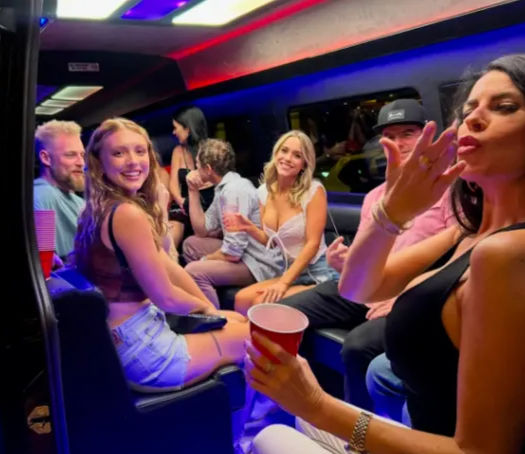 Group of young adults partying inside a stretch limo at night, neon red-and-blue LED lighting, smiling and holding red party cups in a lively, casual atmosphere.