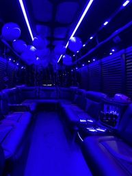 Luxury party bus interior bathed in blue LED lighting, with leather wraparound seating, hanging balloons and ribbon streamers ready for a celebration