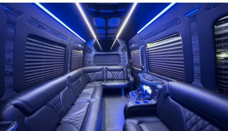 Luxury party van interior with black leather wraparound seating, blue LED ambient lighting, tinted window shades, and built-in cupholders and console.