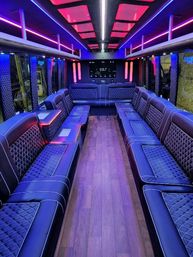 Sleek luxury party bus interior with quilted leather bench seating, wood flooring, and purple-pink LED ceiling lights facing a rear TV