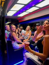 Smiling group of friends partying inside an LED-lit party bus at night, holding red cups and enjoying a lively night out.