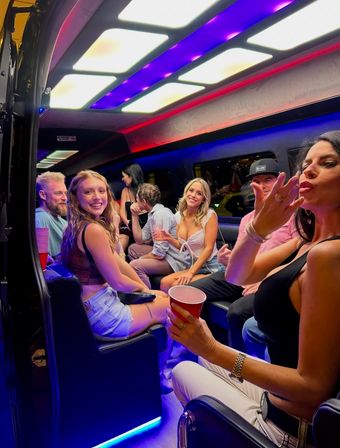 Smiling group of friends partying inside an LED-lit party bus at night, holding red cups and enjoying a lively night out.