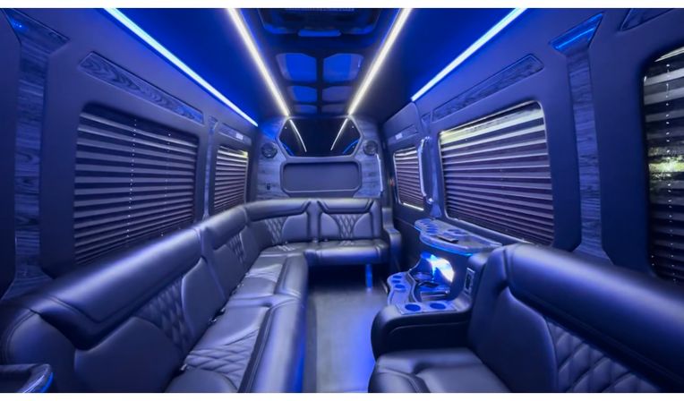 Luxury party bus interior with black leather wraparound seating, blue LED ambient lighting, window blinds and built-in cupholders