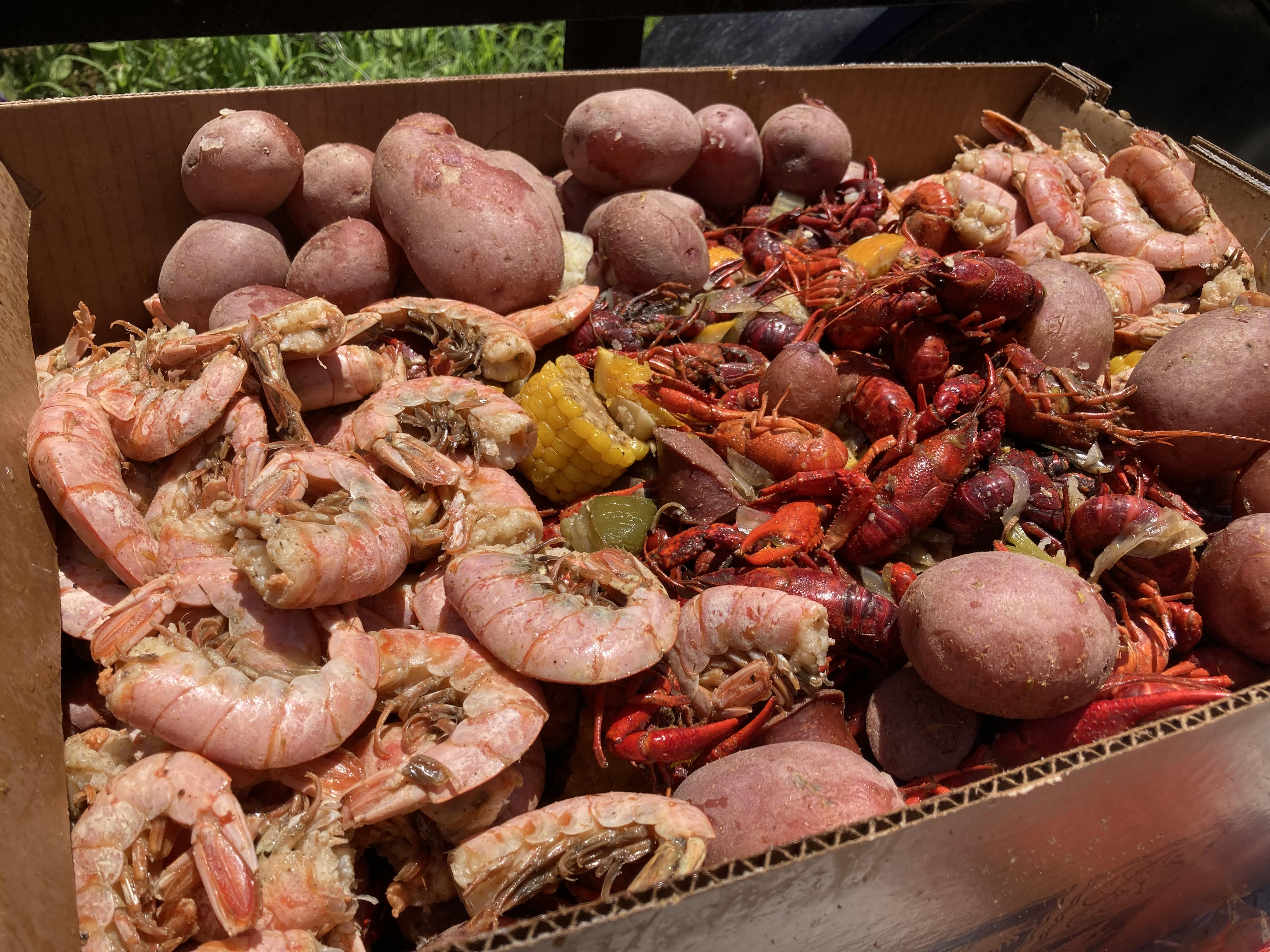Cardboard tray of Southern-style seafood boil with bright red crawfish, pink boiled shrimp, red potatoes and corn on the cob, seasoned Cajun-style.