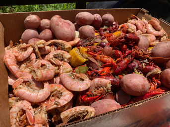 Cardboard tray of Southern-style seafood boil with bright red crawfish, pink boiled shrimp, red potatoes and corn on the cob, seasoned Cajun-style.