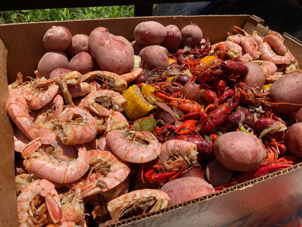 Cardboard tray of Southern-style seafood boil with bright red crawfish, pink boiled shrimp, red potatoes and corn on the cob, seasoned Cajun-style.