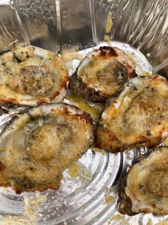 Baked oysters on the half shell with garlic butter, melted cheese and crispy breadcrumbs in a foil tray — savory seafood appetizer