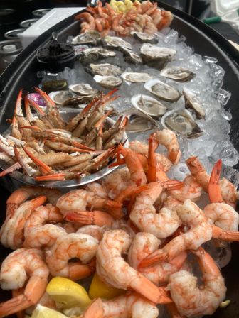 Fresh chilled seafood platter on ice: plump shrimp cocktail with lemon wedges, crab claws, and raw oysters on the half shell — ideal for an oyster bar or seaside market.