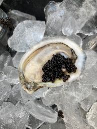 Close-up of a raw oyster half resting on crushed ice, topped with glossy black caviar — fresh seafood appetizer