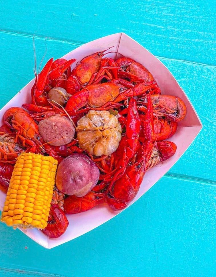 Paper tray of bright red Cajun crawfish boil with corn on the cob, red potatoes, garlic and sausage on a turquoise picnic table