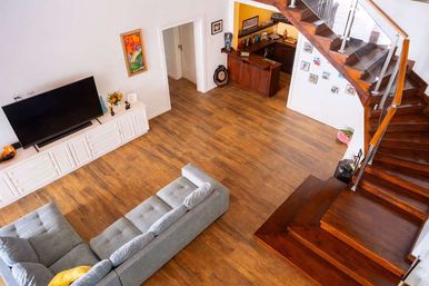 Overhead view of a modern open-plan living room with warm hardwood floors, polished wooden staircase, cozy gray sectional sofa, white TV console and flat-screen TV