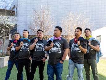 Six friends in matching “Nashville March 2024” t‑shirts with colorful bandanas strike a playful heroic pose in a sunny urban courtyard with leafless trees and a modern building backdrop.