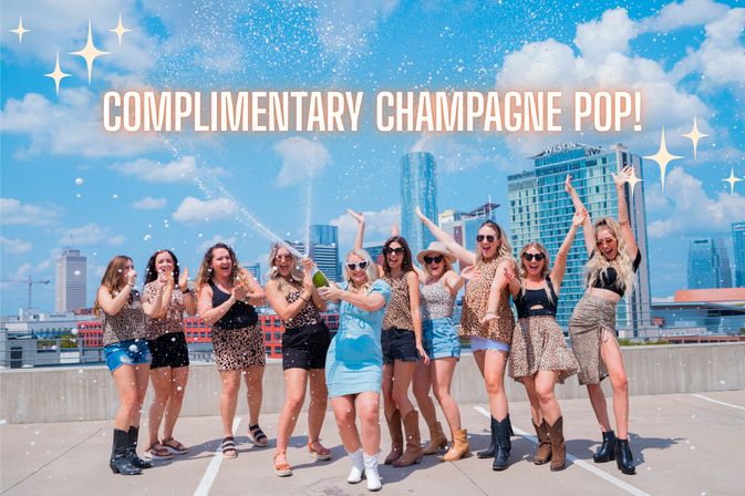 Cheerful group of women on a downtown rooftop parking deck popping champagne and celebrating in summery outfits with a city skyline and blue sky backdrop, large text reading 'COMPLIMENTARY CHAMPAGNE POP!' and festive sparkles.