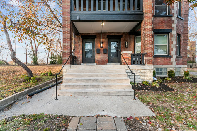 Front entrance of red brick duplex with stone steps, two black doors, porch light and autumn leaves