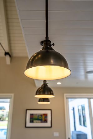 Three black metal dome pendant lights glowing warmly, suspended from a white paneled ceiling in a modern open-concept home interior.