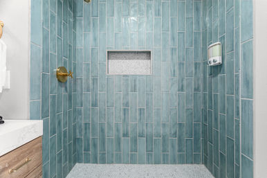 Turquoise vertical subway-tile walk-in shower with brass shower handle, recessed mosaic-tile niche, wall-mounted soap dispenser and hexagon mosaic floor in a modern bathroom.