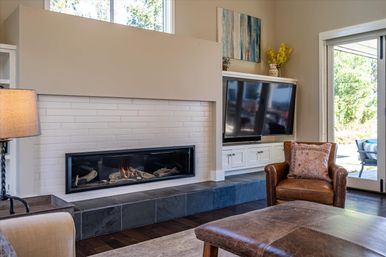 Cozy modern living room with linear gas fireplace, wall-mounted flat-screen TV, leather armchair and sliding glass door to a sunny patio