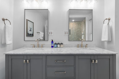 Spa-like modern double-sink bathroom vanity with white marble countertop, gray cabinets, brass faucets, dual mirrors, towels and wall sconces.