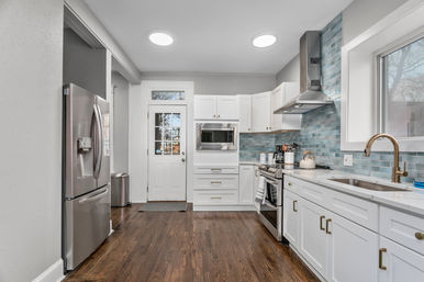 Bright, airy modern kitchen with white shaker cabinets, blue glass subway-tile backsplash, stainless steel appliances, brass faucet, hardwood floors, skylights and a back door