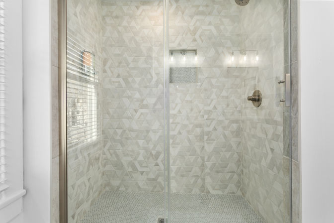 Bright, spa-like walk-in shower with clear glass door, geometric white-and-gray marble wall tiles, pebble mosaic floor, built-in niche, and brushed-nickel shower fixtures