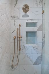Spa-like modern marble shower with brushed gold rainfall head and handheld wand, two recessed niches lined with blue penny tiles and a white herringbone side wall