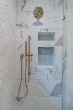 Spa-like modern marble shower with brushed gold rainfall head and handheld wand, two recessed niches lined with blue penny tiles and a white herringbone side wall