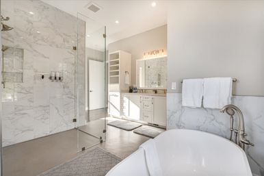 Bright spa-like master bathroom with freestanding soaking tub, chrome fixtures, glass-enclosed marble walk-in shower and white double vanity